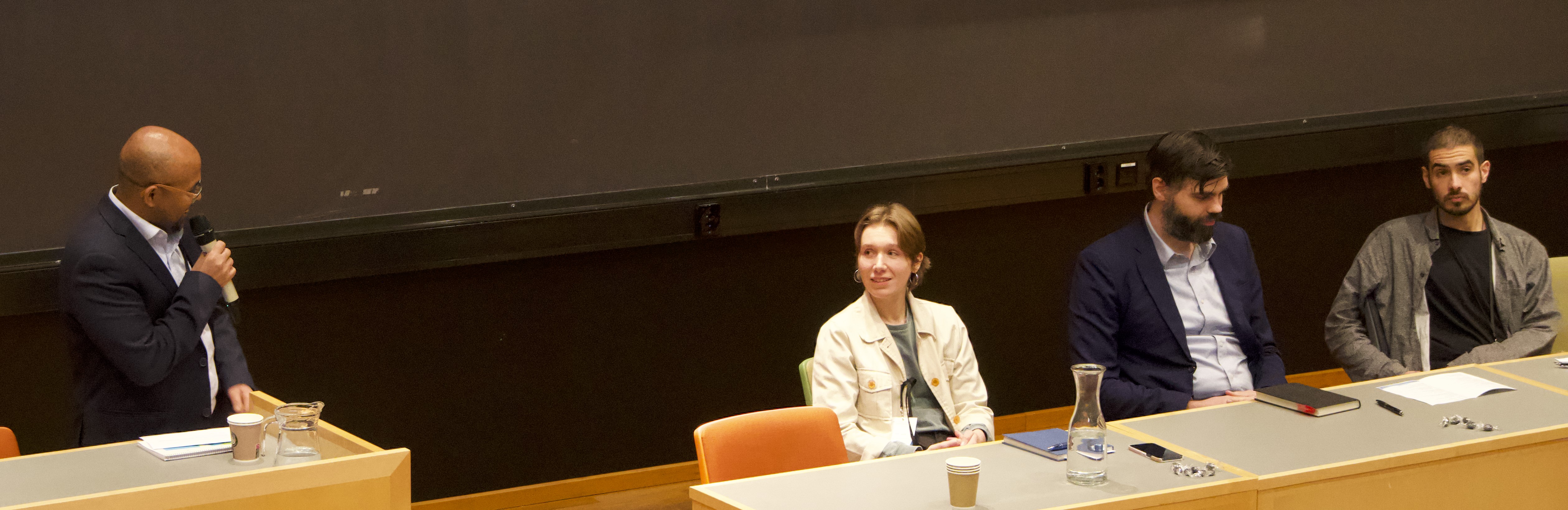 Endalew speaking in the microphone whilst the rest sit next to each other on a row.