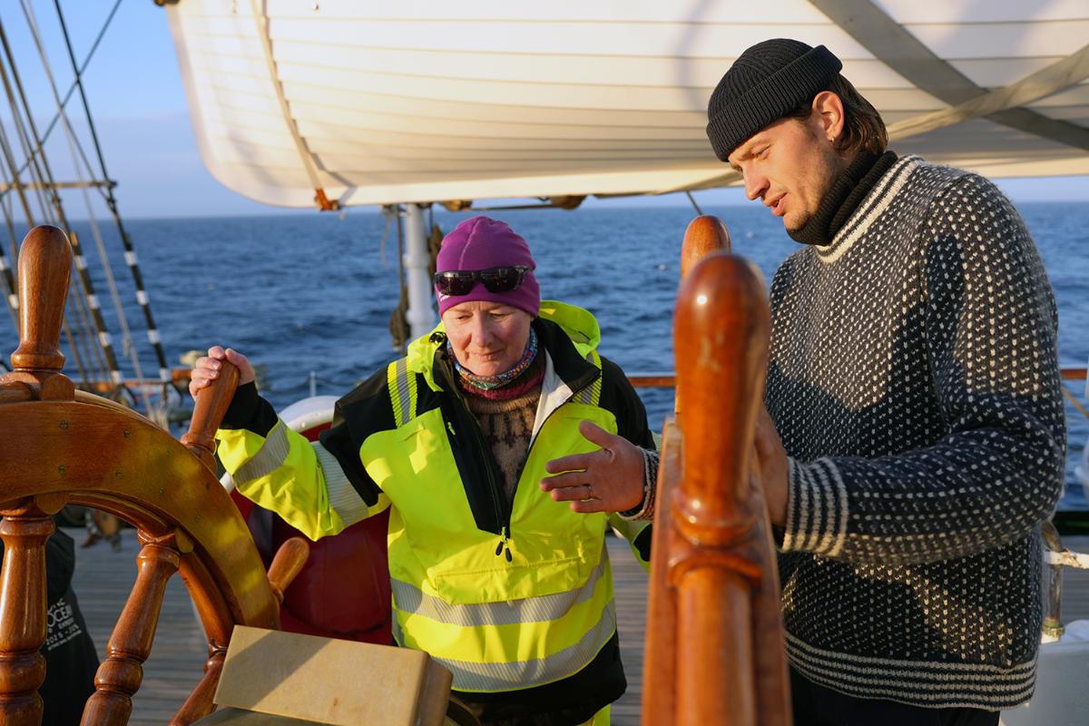 Two persons at the steering wheel on a sail boat