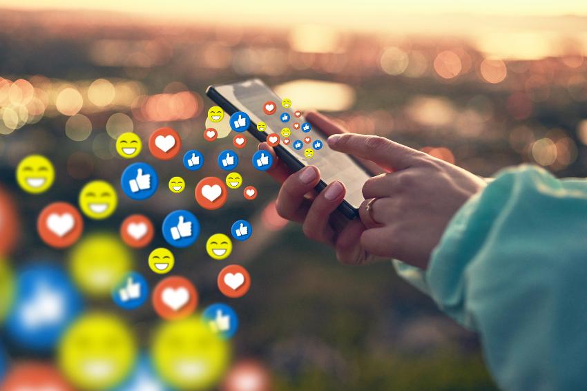 dame som holder telefon i hånda mens emojis flyr rundt i lufta 